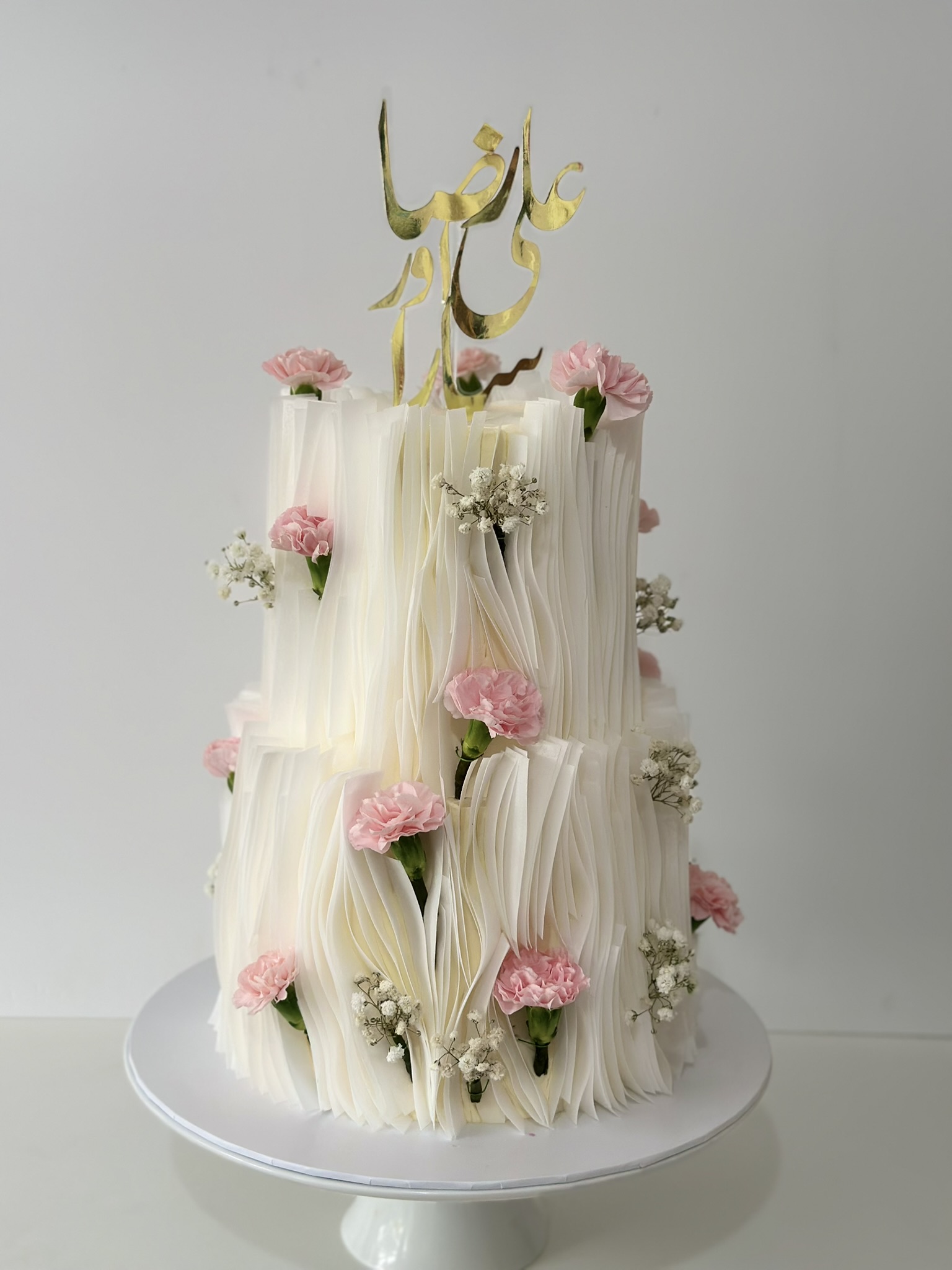 2 tier white ruffled wedding cake with pink carnations side view